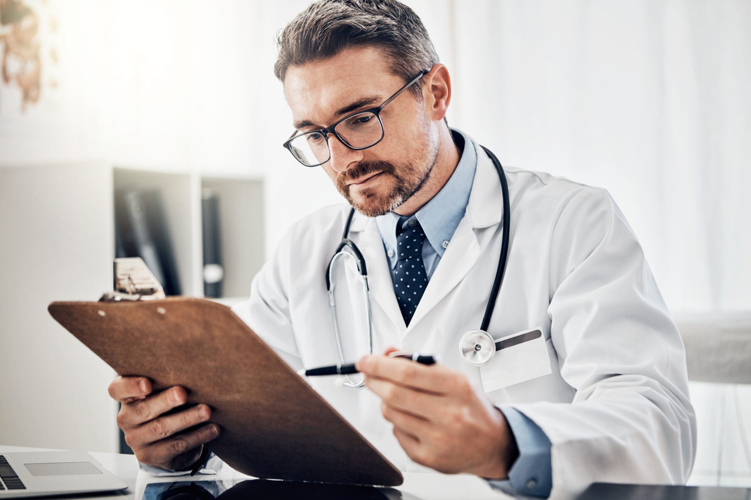 Clipboard, info and doctor in office with healthcare, admin and reading paperwork for results at desk. Thinking, checking and medical professional man with chart, application and health insurance